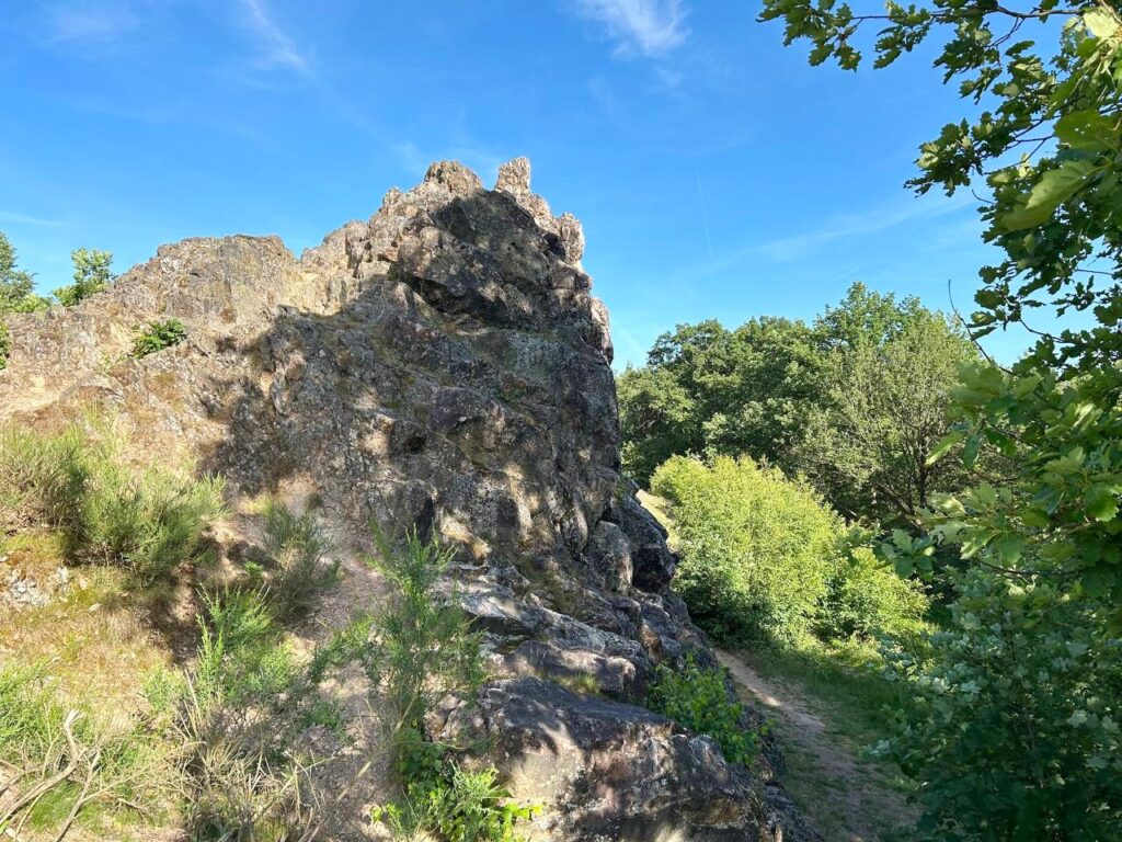 Schroffe graue Felsformation der Eschbacher Klippen, umgeben von grünen Bäumen und Wiese unter tiefblauem Himmel