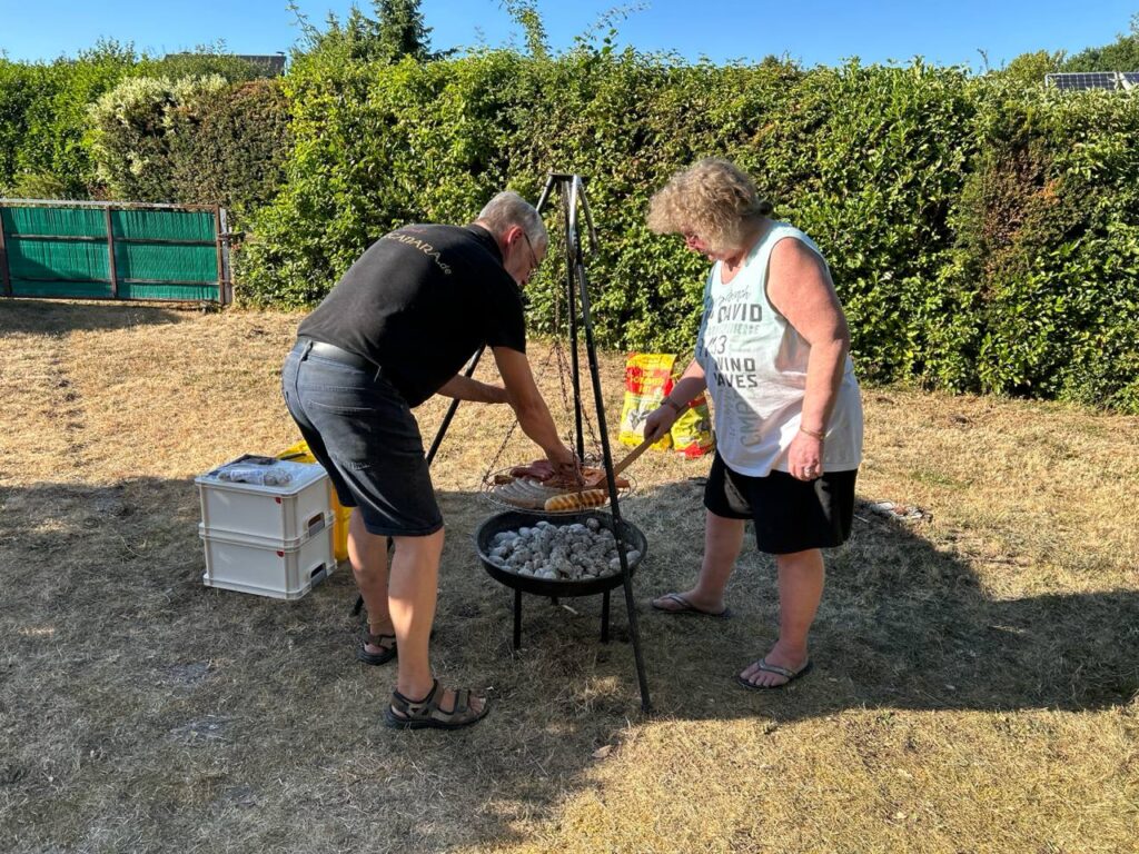 Zwei Teilnehmende legen Grillgut auf den Schwenkgrill